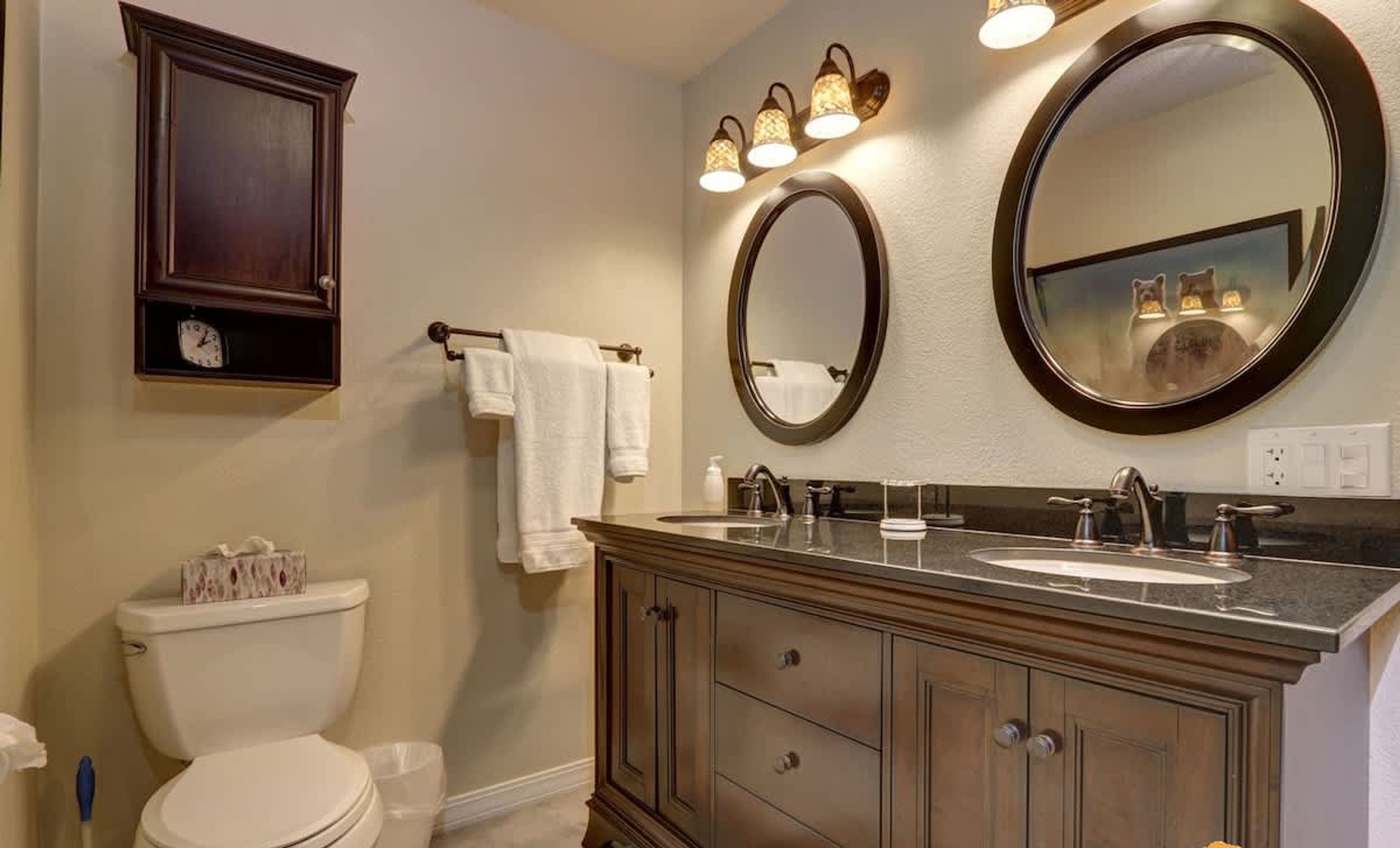 A bathroom with a toilet, a vanity with a sink, two mirrors, and a towel rack.