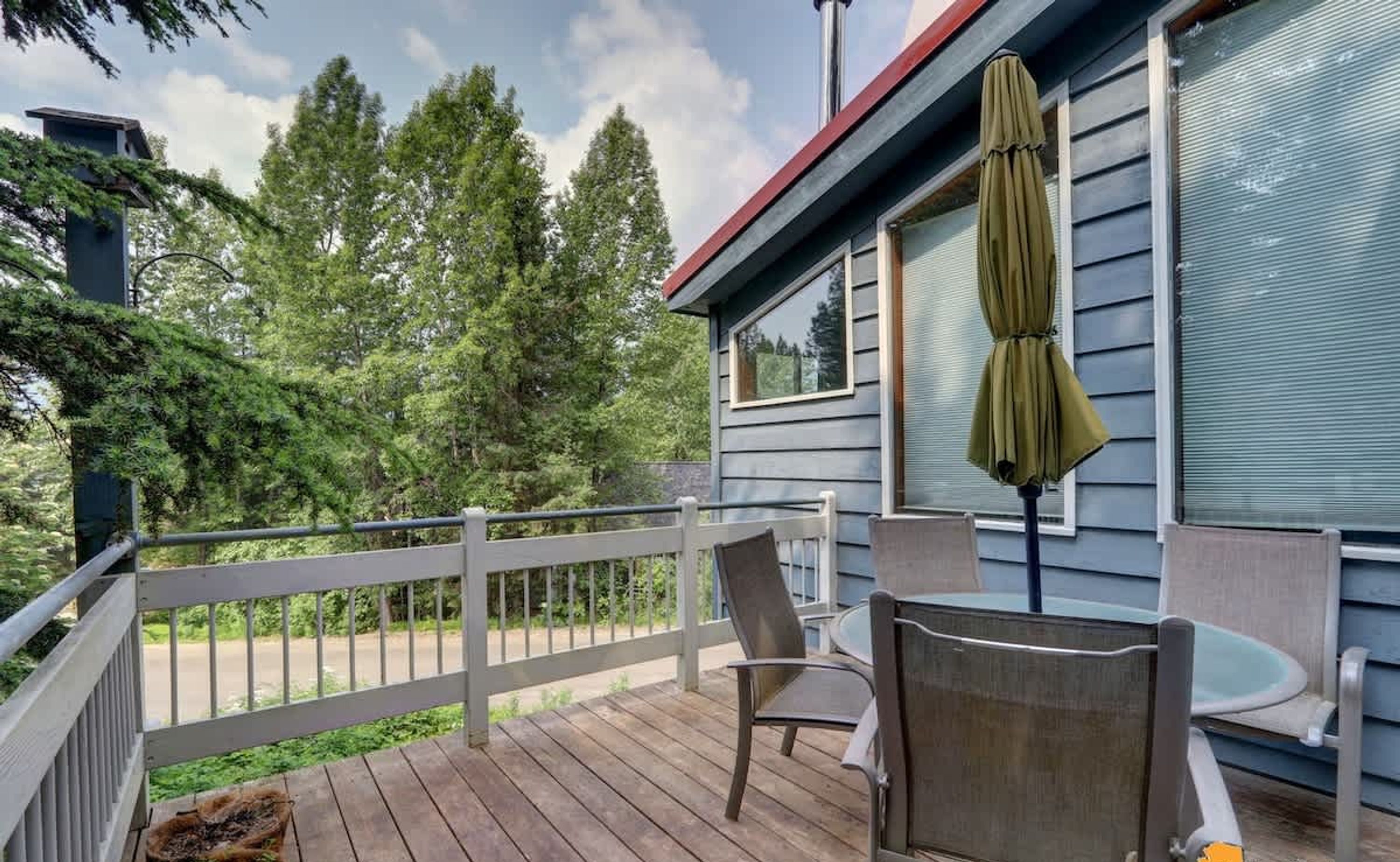 A wooden deck with a white railing, a table, two chairs, and a green umbrella.