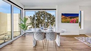 A modern dining area with a marble table, two cushioned chairs, and a large window with a city view. - Luxury 2BR by Oneluxstay (Los Angeles)