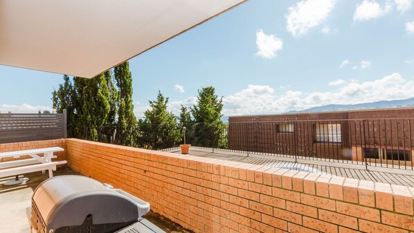 Une terrasse sur le toit avec un barbecue, une table de pique-nique blanche et un mur en briques.