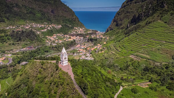 A coastal village with terraced fields, a prominent church with a clock tower, and a clear view of the sea. - Pereira Place Cottage (São Vicente)