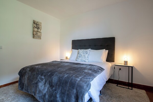 A neatly made bed with a dark headboard, two bedside lamps, and a decorative sign on the wall. - Pereira Place Cottage (São Vicente)