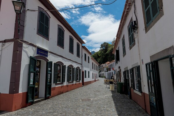 A cobblestone street lined with white buildings with green shutters and a sign for 'OUIFLAP'. - Pereira Place Cottage (São Vicente)
