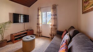 A living room with a wooden ceiling, a flat-screen TV, a sofa, a coffee table, and a potted plant. - Pereira Place Cottage (São Vicente)