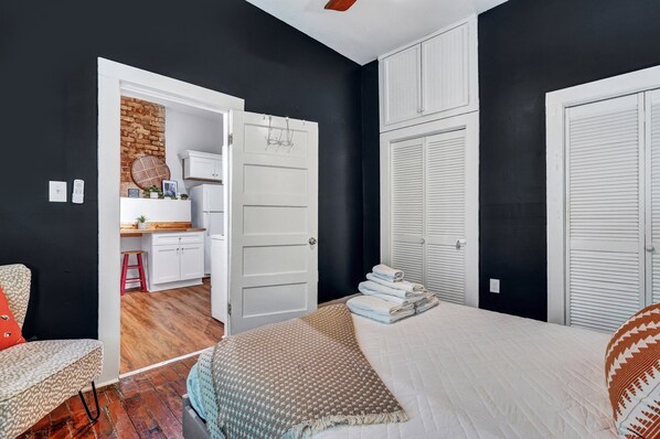 A bedroom with a bed, a desk, and a chair. There is a door leading to another room.