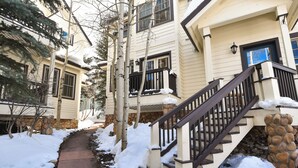 A snow-covered pathway leading to a building with a stone foundation and a wooden staircase. - Mountain Ridge Chalet: Downtown, Hot Tub, Views (Breckenridge)