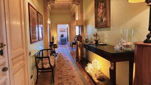 A hallway with a wooden floor, a floral carpet, a desk with a lamp, and framed artwork on the walls. - Domus Gracchi (Rome)