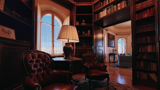 A library with leather armchairs, a lamp, and bookshelves. - Domus Gracchi (Rome)