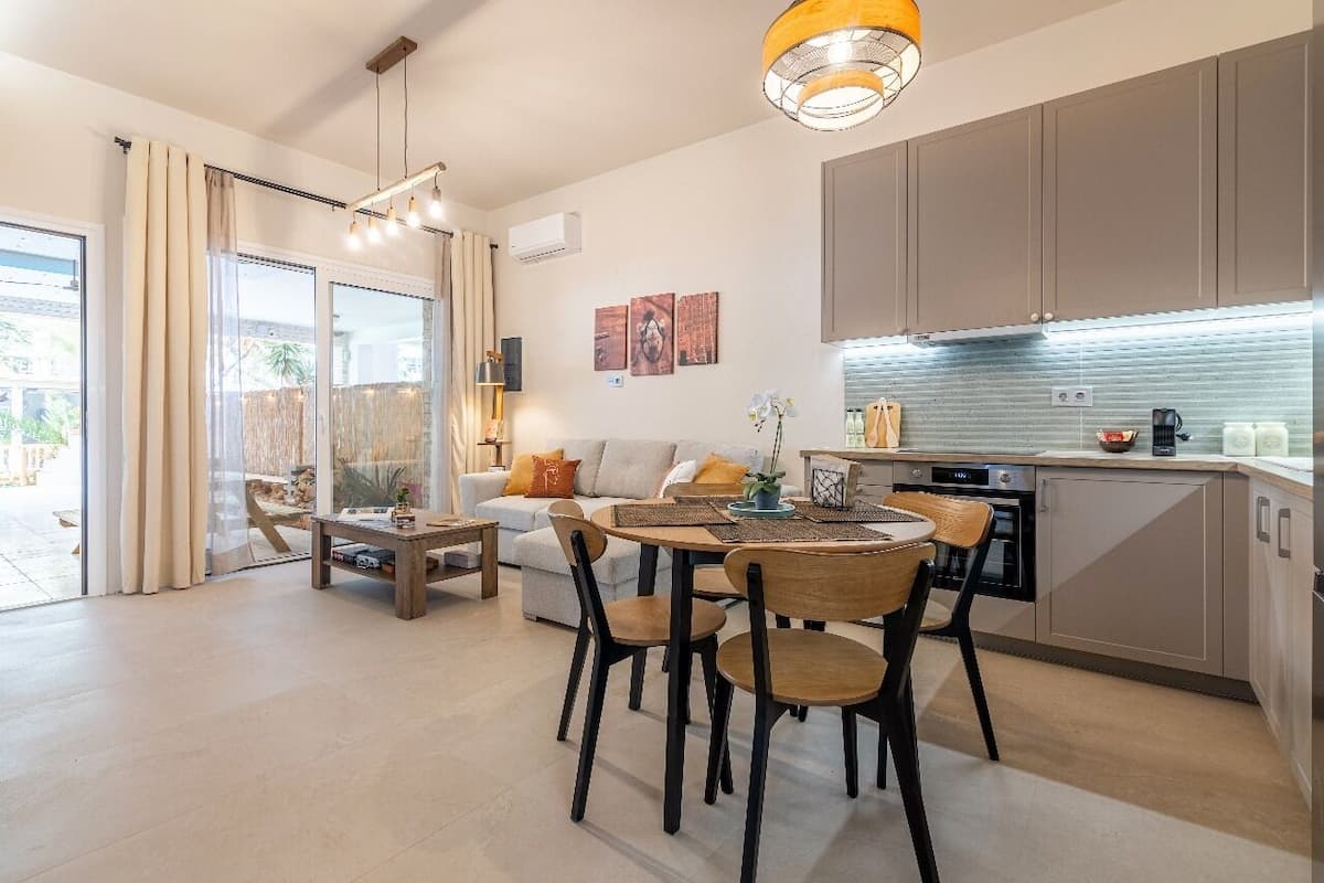 A modern living room with a sofa, coffee table, and dining area. There is a kitchen with cabinets and appliances.