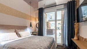A bedroom with a bed, a nightstand, a TV, and a sliding glass door leading to an outdoor area. - Petra - Stylish Apartment (Hersonissos)