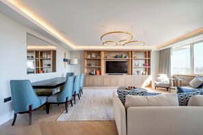 Ein modernes Wohnzimmer mit Essbereich, einer Sofagarnitur, einem Fernseher und einem großen Fenster.