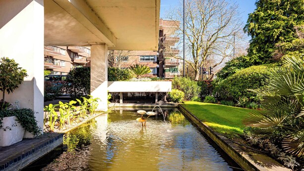 Un pati tranquil amb una font, envoltat de vegetació exuberant i un edifici amb balcons.