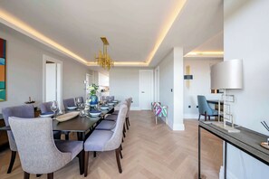 A modern dining area with a long table, chairs, and a chandelier.