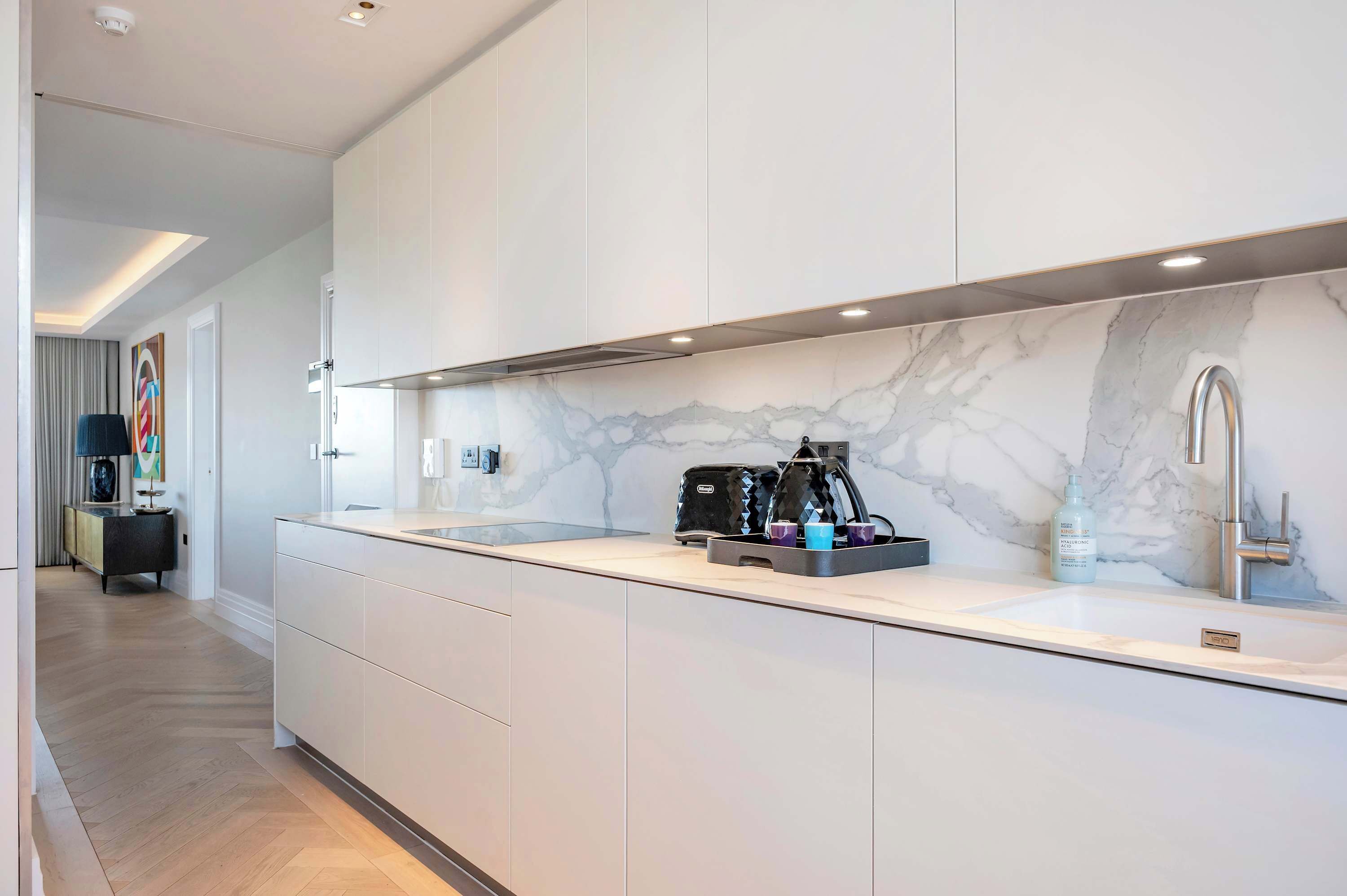 Een moderne keuken met witte kasten, een marmeren achterwand en een inbouwgootsteen.
