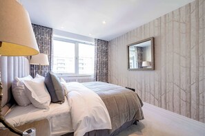 Un dormitorio con cama, ventana, lámpara y espejo en la pared.