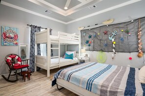 Ein Zimmer mit einem Etagenbett, einem Schaukelstuhl, einem Bett mit gestreifter Decke und einer Wand, die mit maritimen Dekorationen versehen ist.