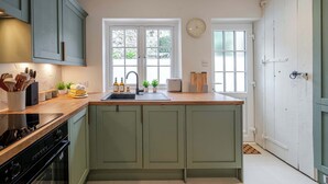 A kitchen with green cabinets, a wooden countertop, a sink, and a window with a view of greenery outside.