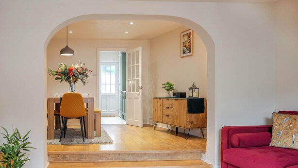 A modern living room with a red sofa, wooden dining table with chairs, and a staircase leading to another room.