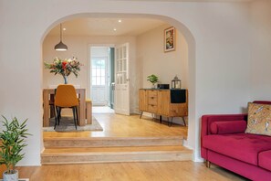 A modern living room with a red sofa, wooden dining table with chairs, and a staircase leading to another room. - Kaolin: Splendid Cornwall Home by STAE-Homes (St Austell)