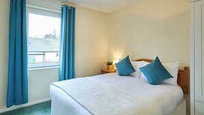 Habitación de hotel con cama, cortinas, mesita de noche con lámpara y vistas al exterior.