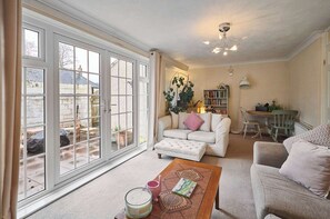 A living room with a white sofa, a wooden coffee table, and a dining area with a table and chairs. - Host & Stay | Trinity Way (Keswick)