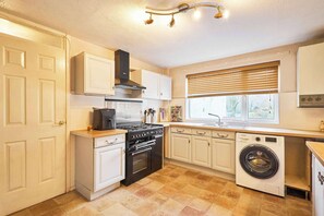 A compact kitchen with a stove, oven, microwave, and washing machine. - Host & Stay | Trinity Way (Keswick)