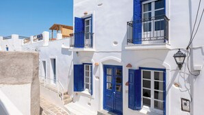 A white building with blue shutters and a balcony, a stone staircase, and a small window with a light fixture. - Marouso Villa - Paros Seaview Getaway (Marpissa)