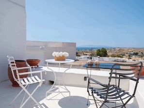A balcony with a white metal chair, a wicker basket with white flowers, and terracotta pots.