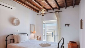 A bedroom with a bed, a bedside lamp, a wooden ceiling, a window with curtains, and a large terracotta pot. - Marouso Villa - Paros Seaview Getaway (Marpissa)