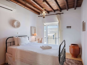 A bedroom with a bed, a bedside lamp, a wooden ceiling, a window with curtains, and a large terracotta pot. - Marouso Villa - Paros Seaview Getaway (Marpissa)