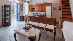 A spacious room with a wooden ceiling, a dining area with a table set for two, a kitchen with wooden cabinets, and a staircase leading to an upper level. - Marouso Villa - Paros Seaview Getaway (Marpissa)