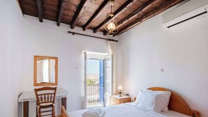 A bedroom with a wooden bed, a desk with a chair, a mirror, and a balcony with a view. - Marouso Villa - Paros Seaview Getaway (Marpissa)