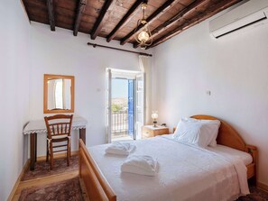 Un dormitorio con una cama de madera, un escritorio con una silla, un espejo y un balcón con vistas.