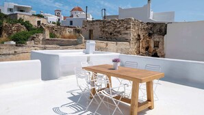 A rooftop terrace with a wooden table and white chairs, overlooking a white-washed building with red-tiled roofs and stone walls. - Marouso Villa - Paros Seaview Getaway (Marpissa)