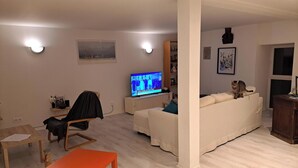 Ein Wohnzimmer mit Fernseher, einer Couch, einem Sessel und einem Tisch.