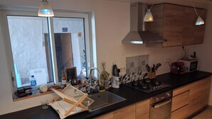 Eine moderne Küche mit Holzschränken, einer schwarzen Arbeitsplatte, Edelstahlgeräten und Pendelleuchten.