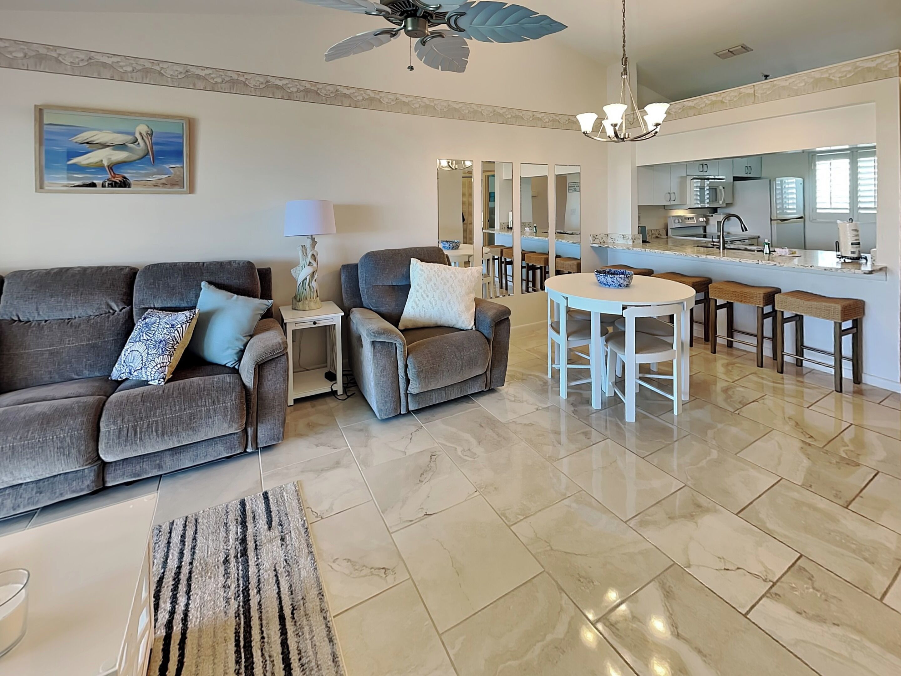 A modern living room with a grey sofa, a small side table, and a dining area with a white table and bar stools.