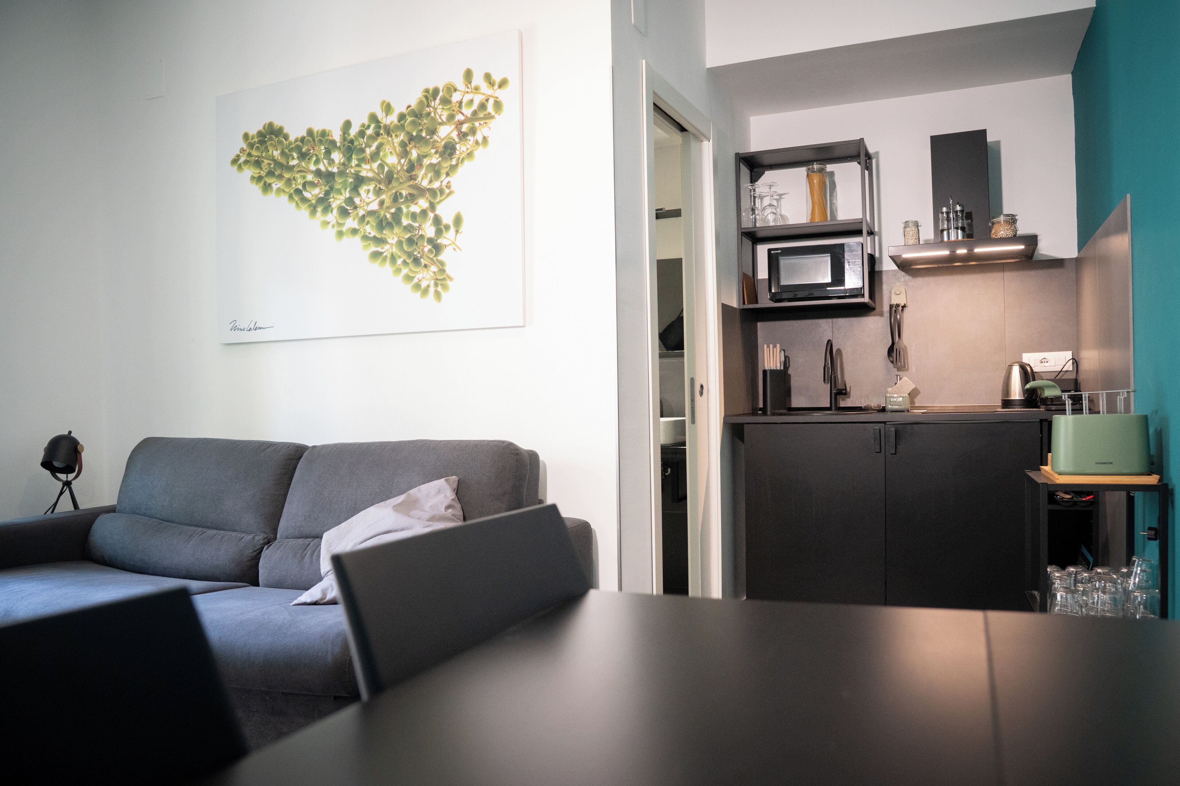Un espace de vie moderne comprenant un canapé gris, une table à manger, un coin cuisine avec un four à micro-ondes et une œuvre d’art encadrée accrochée au mur.