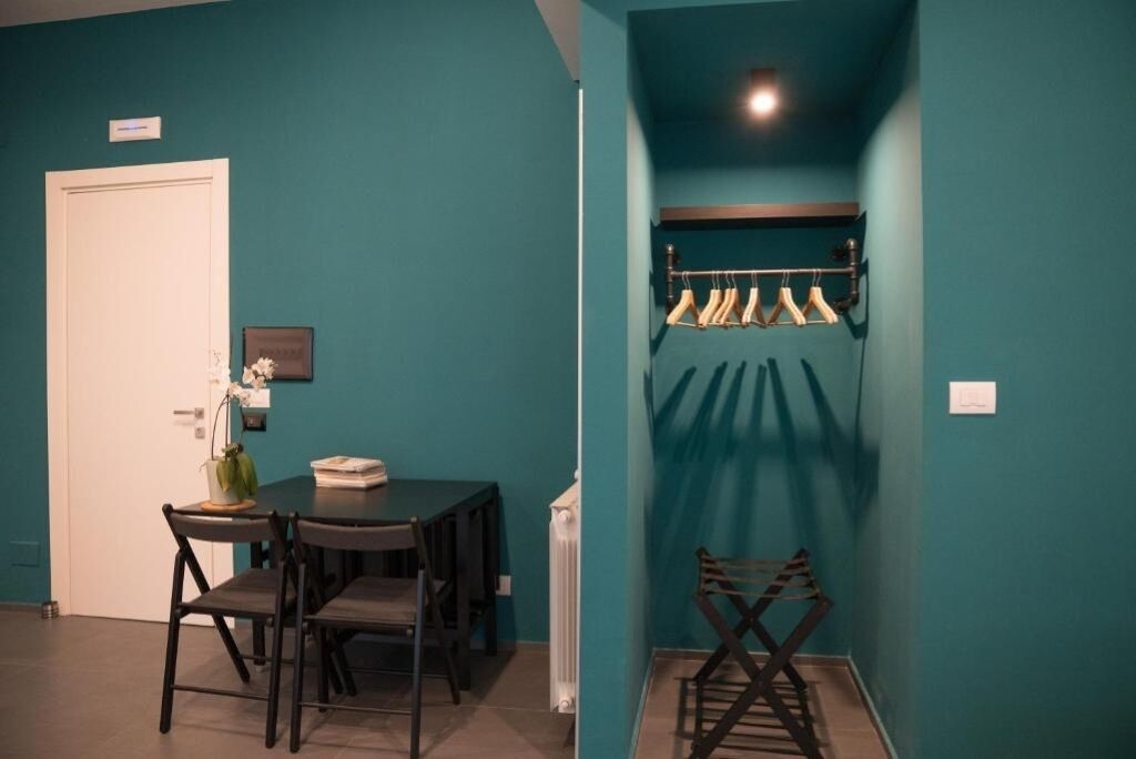 Une pièce aux murs de couleur turquoise, une table à manger avec des chaises, un porte-manteau avec des v êtements suspendus et une porte blanche.