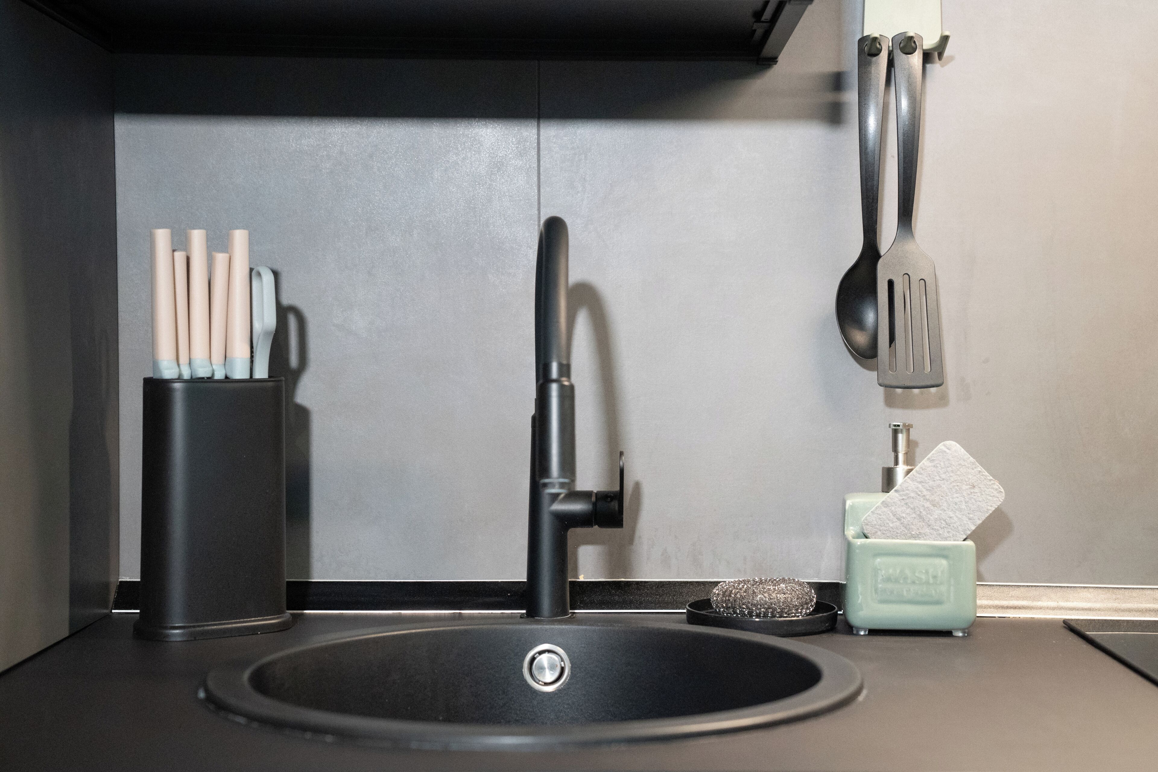 A modern kitchen sink with a faucet, a dish soap dispenser, and a utensil holder.