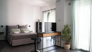 Quarto moderno com cama, escrivaninha, televisão e planta em vaso.