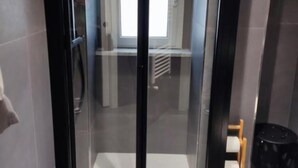 Um elevador moderno com portas de vidro, corrimão visível e uma pequena lixeira à direita.