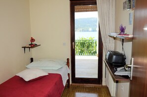 A bedroom with a bed, a small shelf with a lamp, a door leading to a balcony, and a desk with a printer. - Spacious Seaside Retreat in Poljica (Marina)