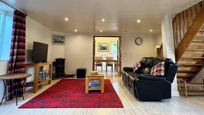 A living room with a sofa, a television on a stand, a red rug, and a staircase.