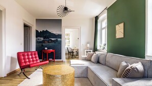 A modern living room with a red chair, a beige sofa, a stone coffee table, and a mountain landscape painting on the wall. - HohnsteinOase-Infrared Sauna-3 Bedroom-Parking and washing machine (Hohnstein)
