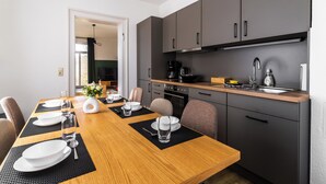 A modern kitchen with grey cabinets, a wooden dining table set for four, and a visible coffee machine. - HohnsteinOase-Infrared Sauna-3 Bedroom-Parking and washing machine (Hohnstein)