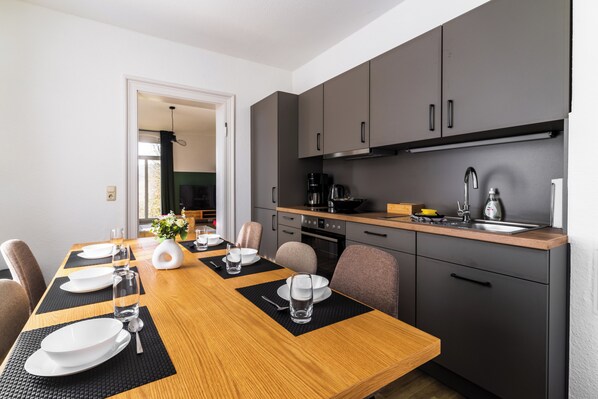 A modern kitchen with grey cabinets, a wooden dining table set for four, and a visible coffee machine. - HohnsteinOase-Infrared Sauna-3 Bedroom-Parking and washing machine (Hohnstein)