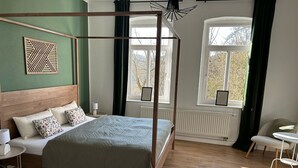 A four-poster bed with a wooden headboard, a round white table, and a chair with a white cushion. - HohnsteinOase-Infrared Sauna-3 Bedroom-Parking and washing machine (Hohnstein)