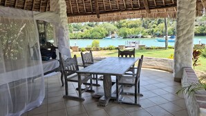 Un espacio al aire libre techado con mesa y sillas, con vista a una masa de agua y follaje.
