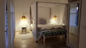 Una cama con dosel, lámparas de noche, una mesita y un banco.